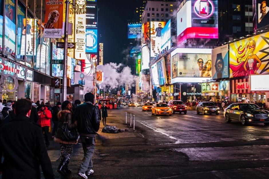 An image of a well lit, busy high street. The street is full of stores and billboard advertisements can be seen.