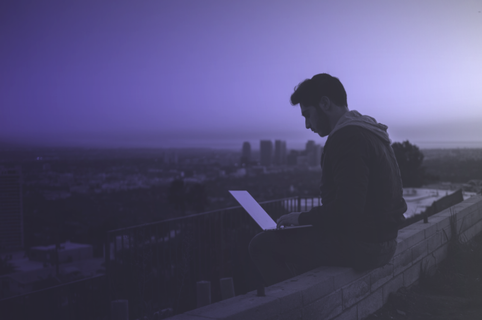 Mann sitzt mit Laptop auf einer Mauer