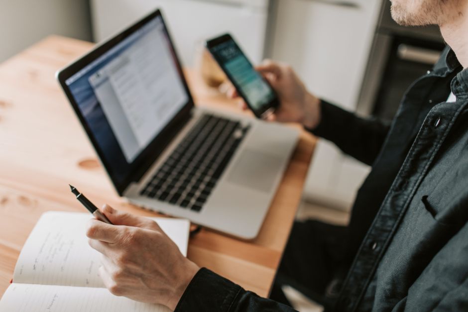 Person hält ein Handy in der einen Handy und sitzt am Laptop