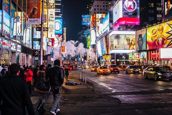 An image of a well lit, busy high street. The street is full of stores and billboard advertisements can be seen.