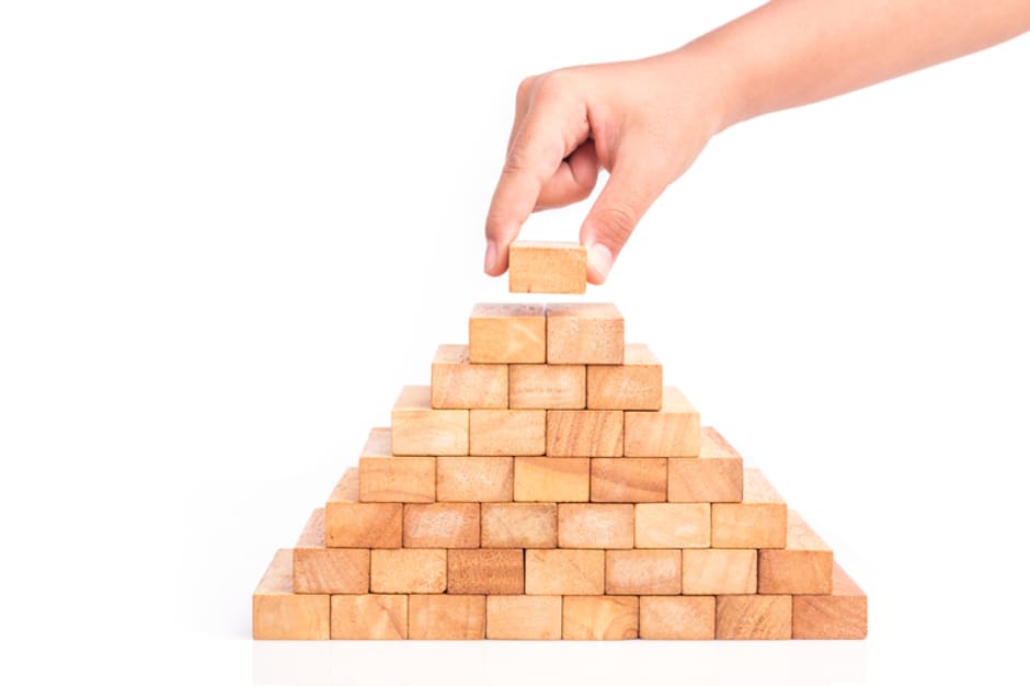 An image of a final wooden building block being placed at the top of a pre-built pyramid shape alluding to building an affiliate marketing strategy.