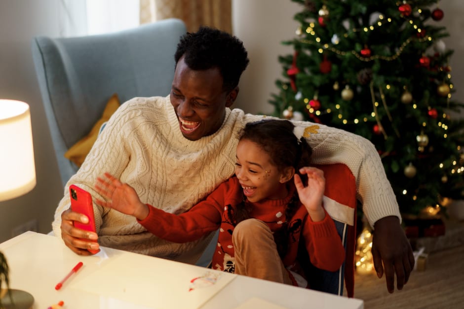 Vater und Tochter in Weihnachtspullovern schauen lachend aufs Smartphone