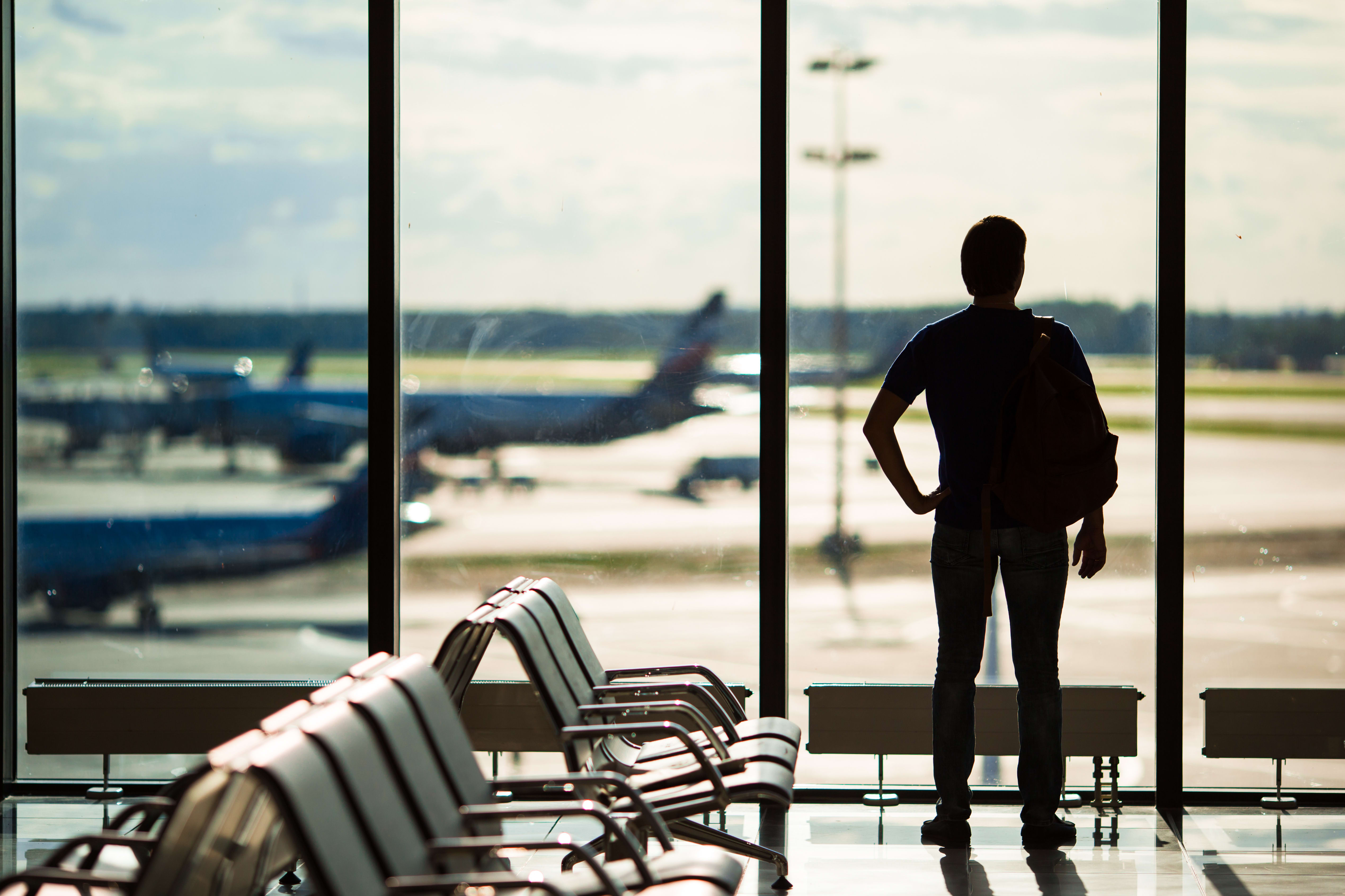 Man op een vliegveld, kijkend uit het raam naar vliegtuigen