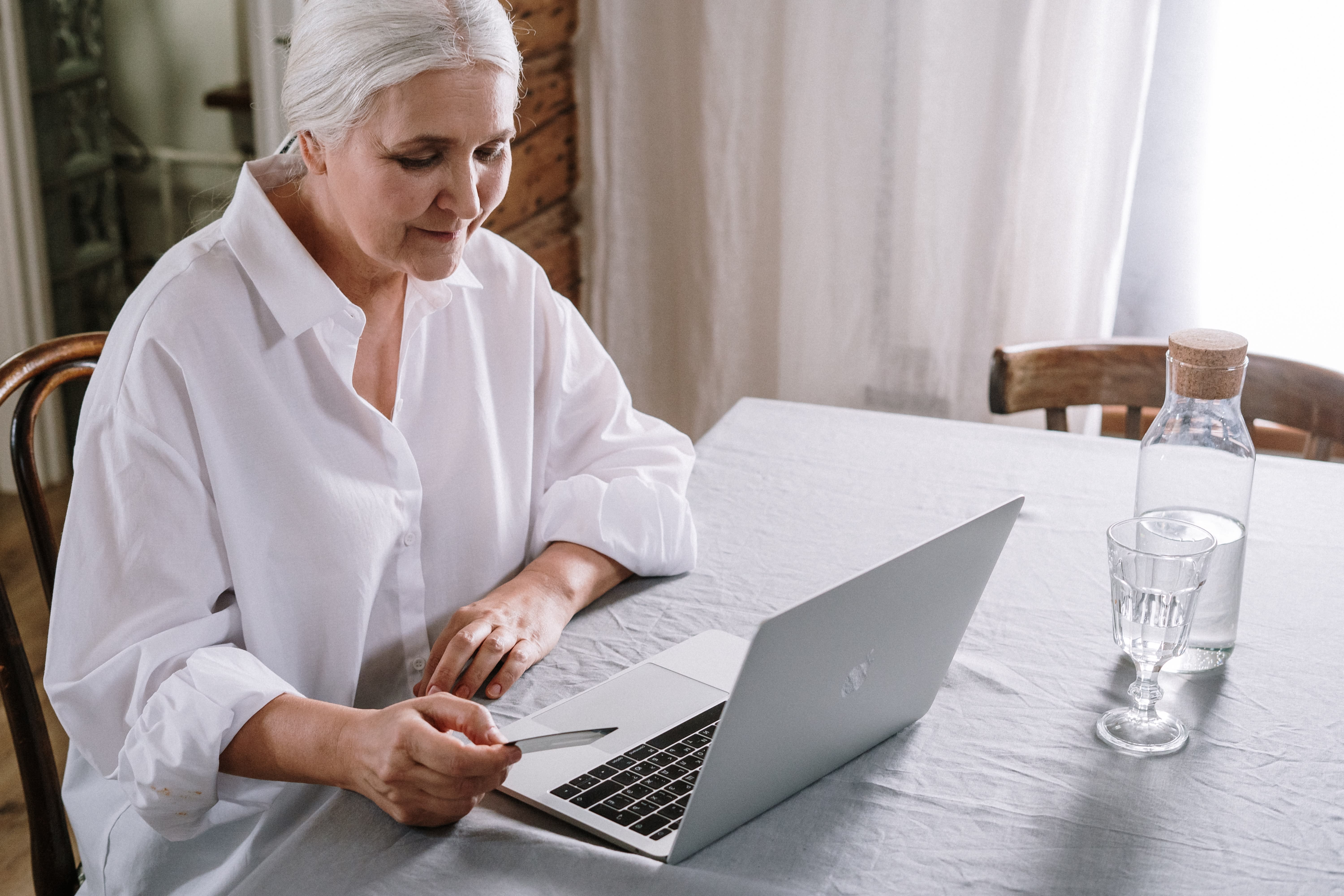 ältere Dame sitzt am Laptop und hält Kreditkarte in der Hand