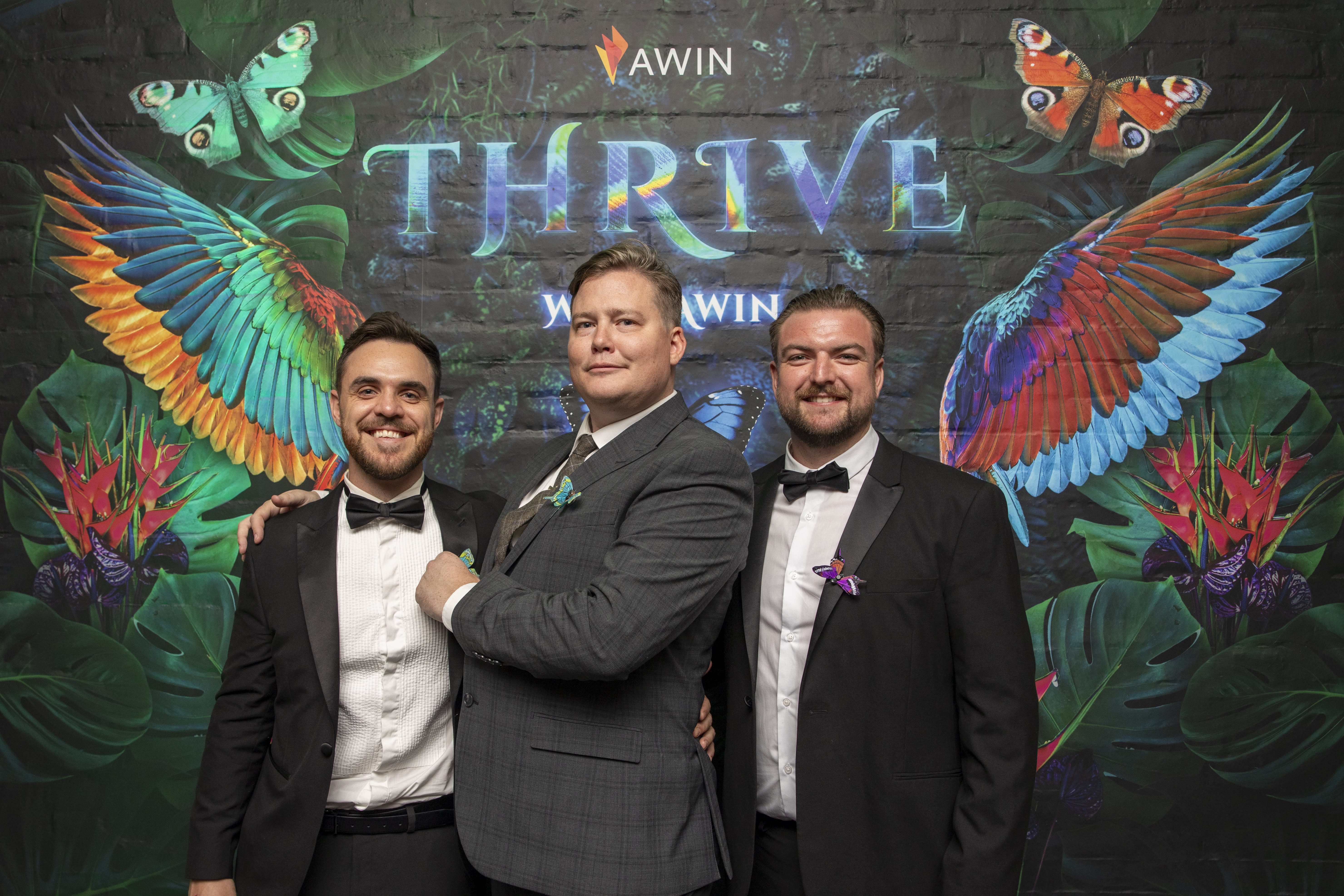 Three guests in Black-Tie attire stand in front of a jungle-themed photo wall that reads 